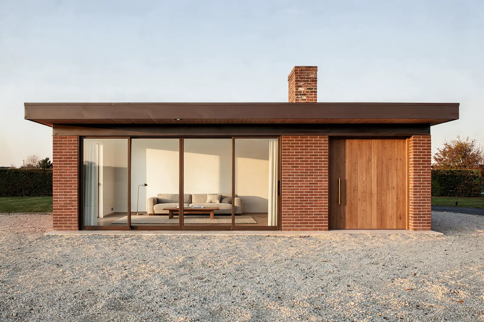 The same house today: a flat roof with an oak soffit, warm clay render, a run of full-height glass, oak slatted doors where the garage was, and the original brick chimney.