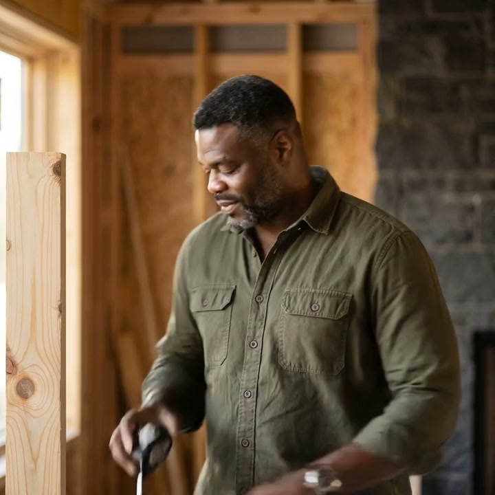 Jonas Oduya on site in an olive work shirt, timber framing and a basalt wall behind him.